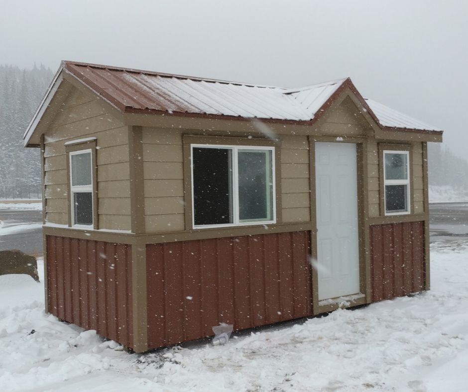 Tan and red storage shed with a snow-rated metal roof in falling snow at a Colorado mountain property
