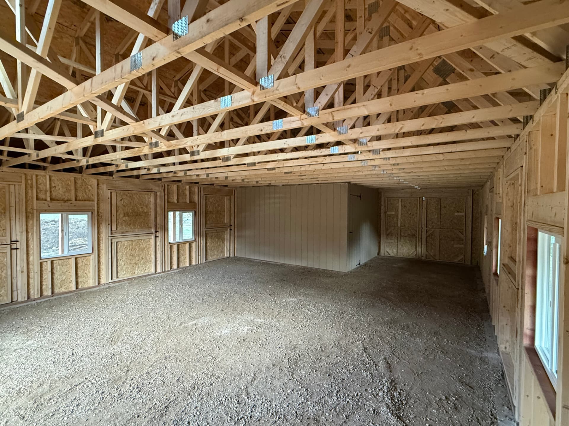 Interior of a custom barn in Parshall showing trusses, framed walls, gravel floor and enclosed tack room area