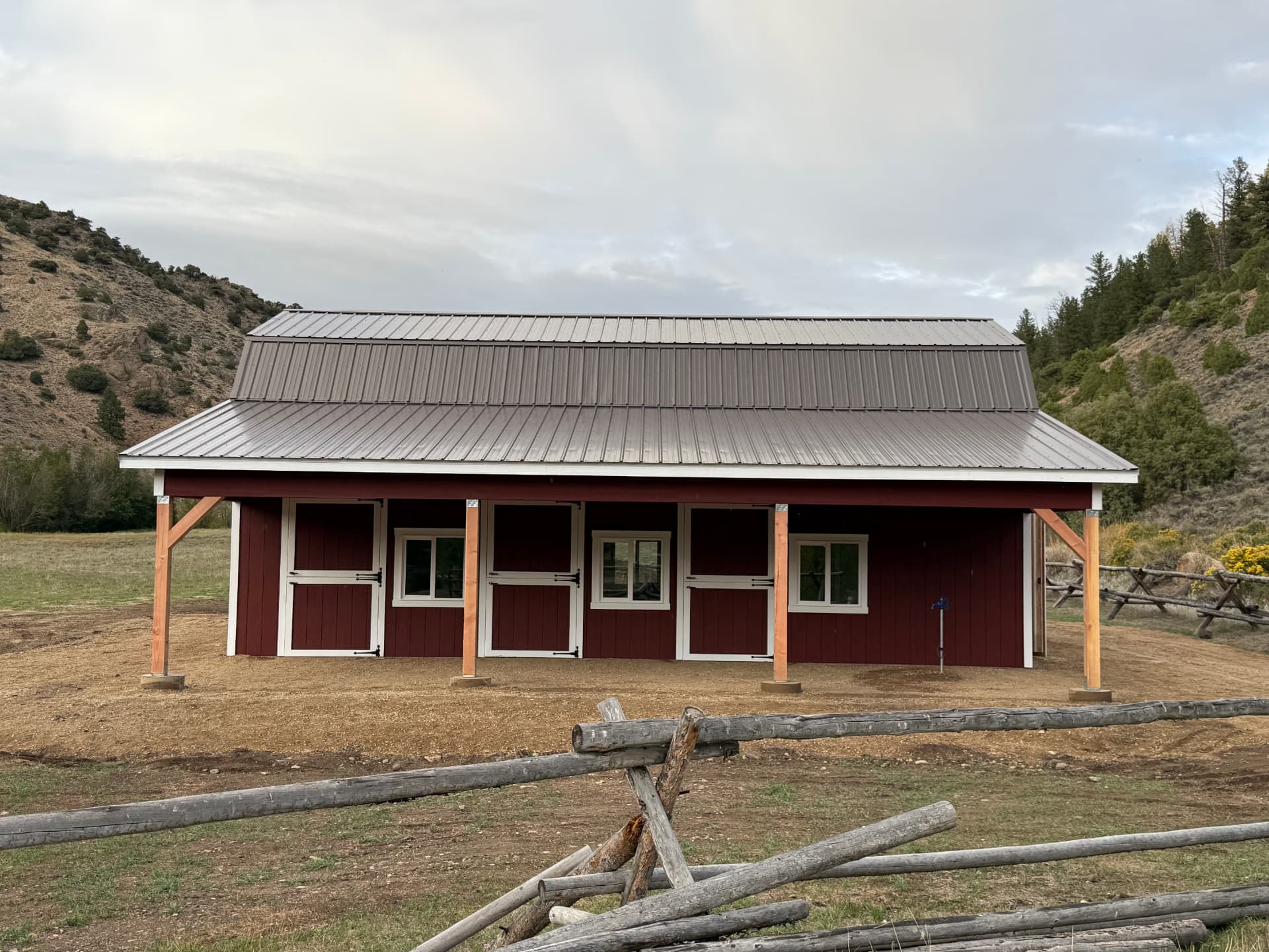 Finished custom red barn with metal roof, multiple stall doors and covered eave overhang in Parshall, Colorado