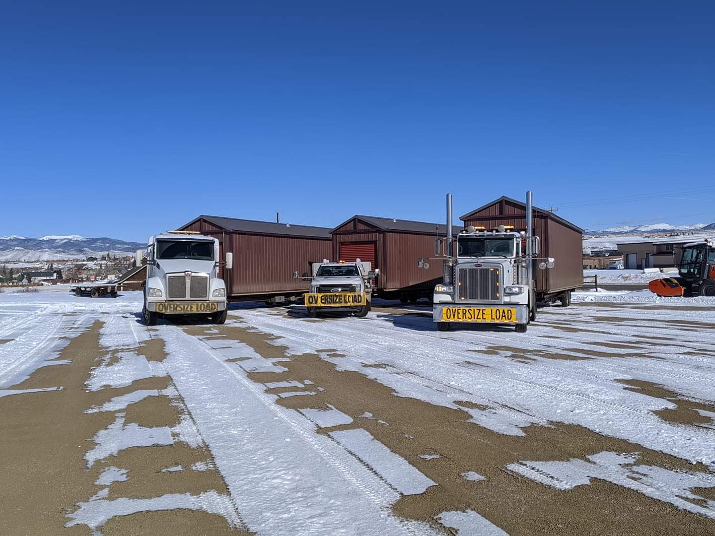 Oversize-load trucks transporting fully assembled prefab garages in winter conditions