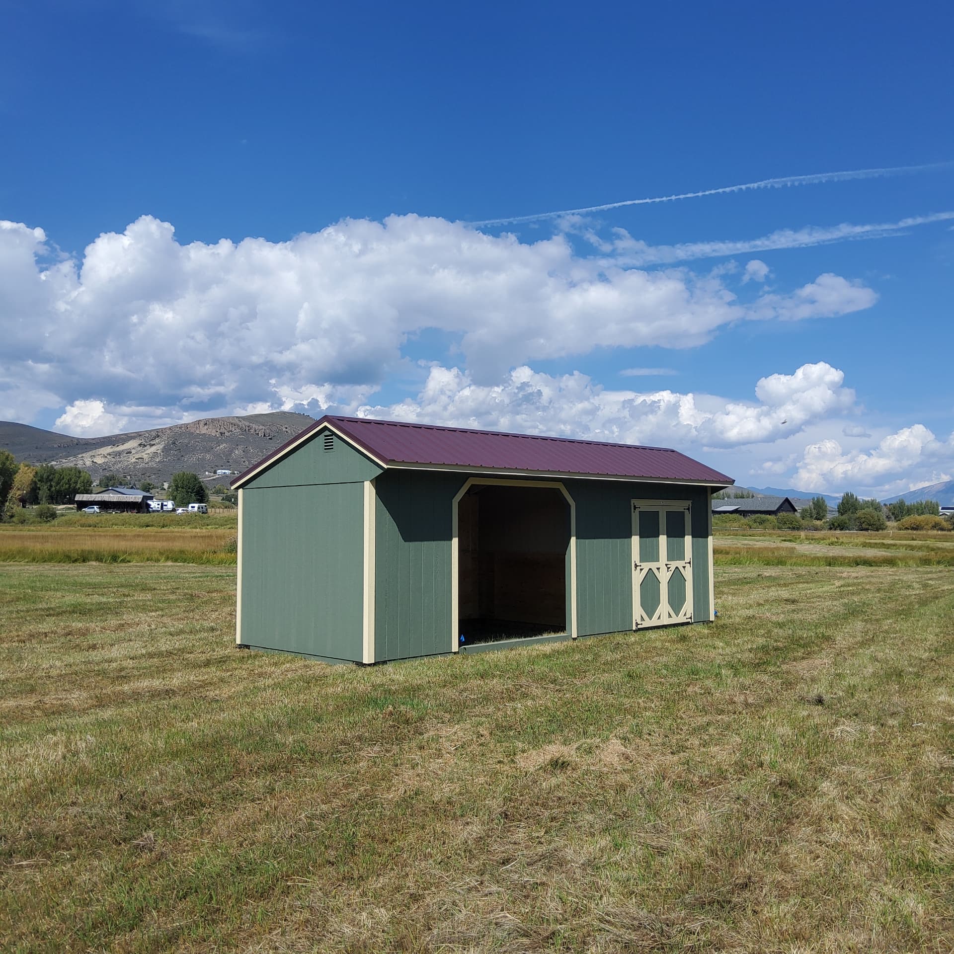 Green loafing shed with maroon roof and white trim installed on a Colorado ranch with open front and side door
