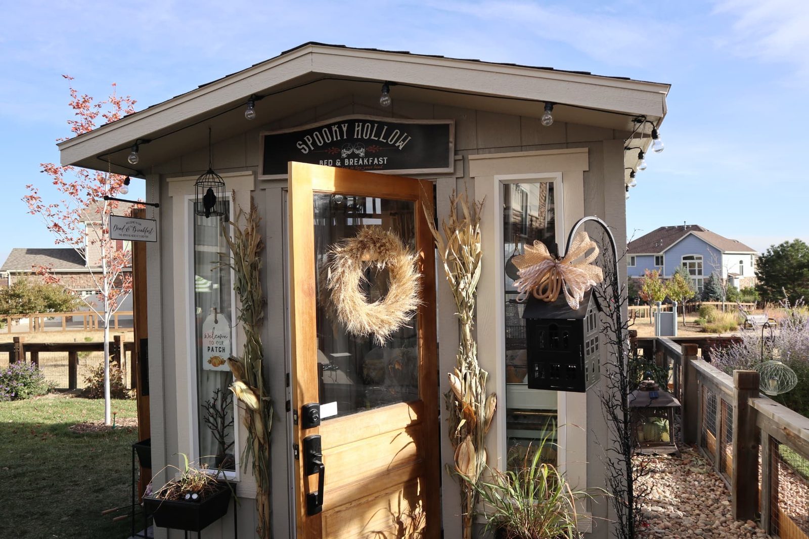 Front exterior of a finished 8x10 Classic A-Frame She Shed in Aurora, CO, decorated for fall with open wood doors