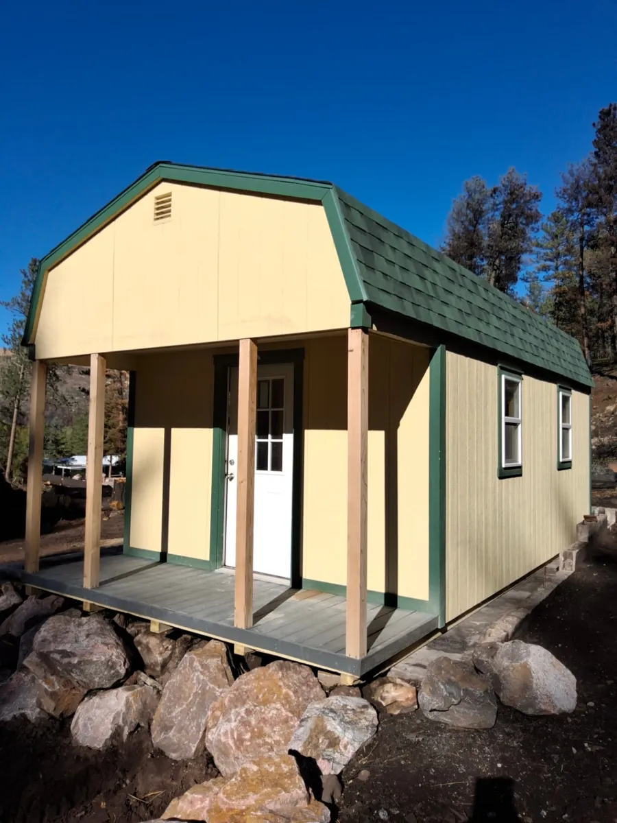 Front of a used Hi Wall Barn with gambrel roof, four cedar porch posts, composite porch floor and white 9-lite door in Beulah, Colorado