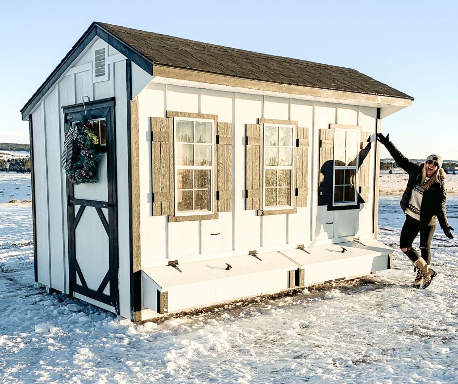 Customer beside a white chicken coop with shutters and nesting boxes standing up to snow in Colorado