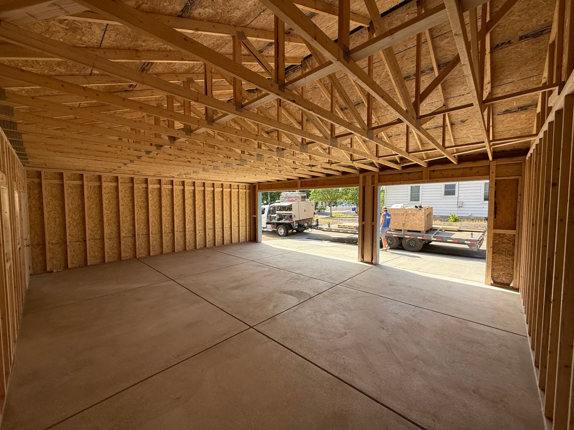 Unfinished framed interior of the Greeley 24×30 garage looking toward its two open overhead-door bays and concrete floor