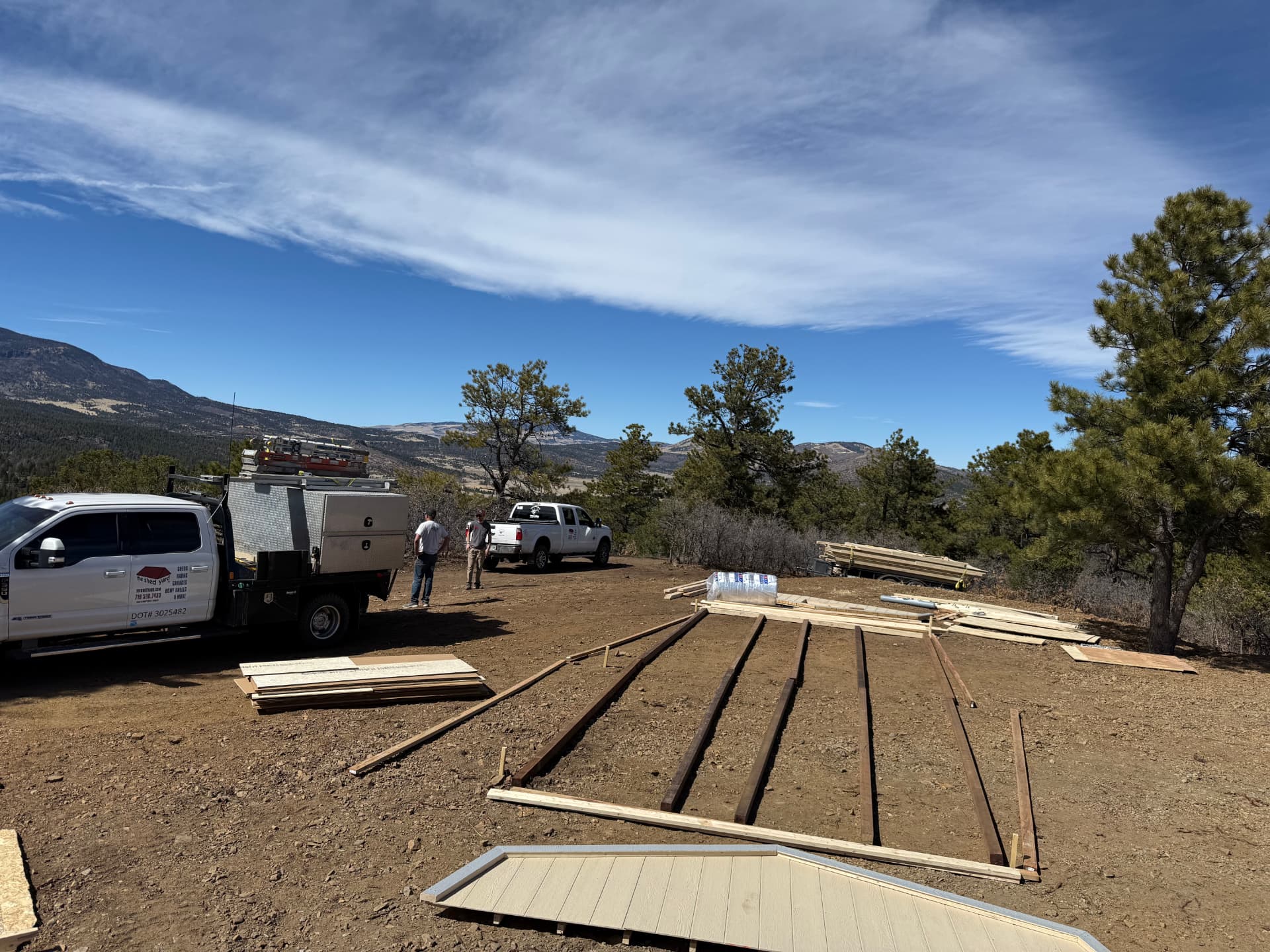 Shed Yard trucks at a hilltop job site near Canon City with 4x4 pressure-treated runners laid out for a 14x32 barn