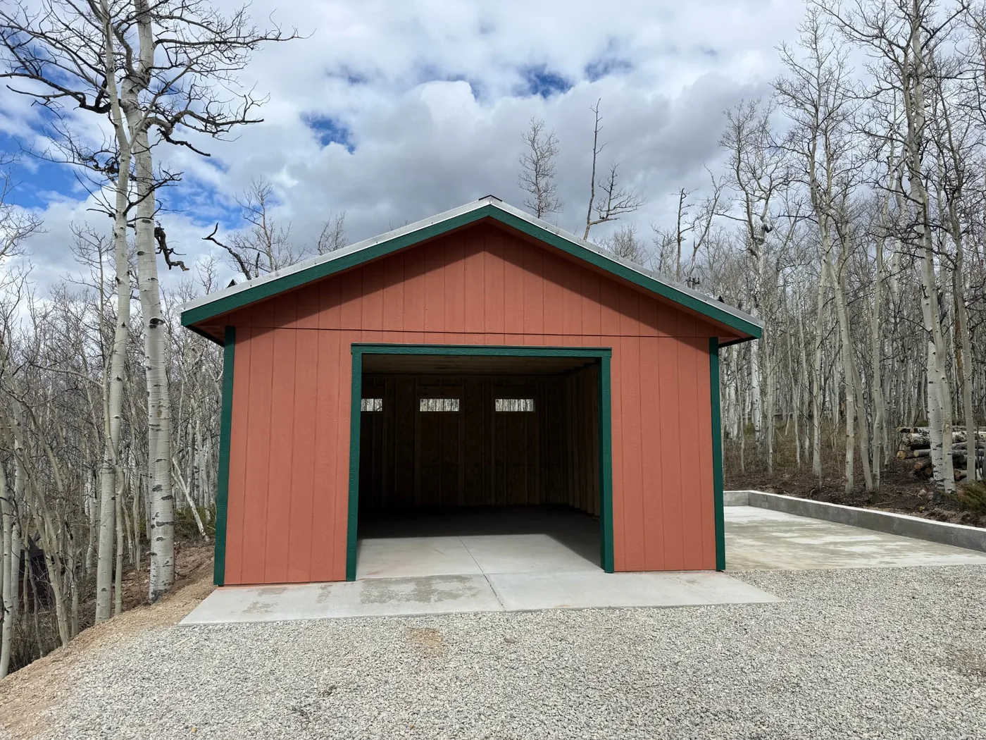 Terracotta 16x20 garage with dark green trim and a corrugated metal roof at a wooded Jefferson, Colorado property, with a concrete front apron