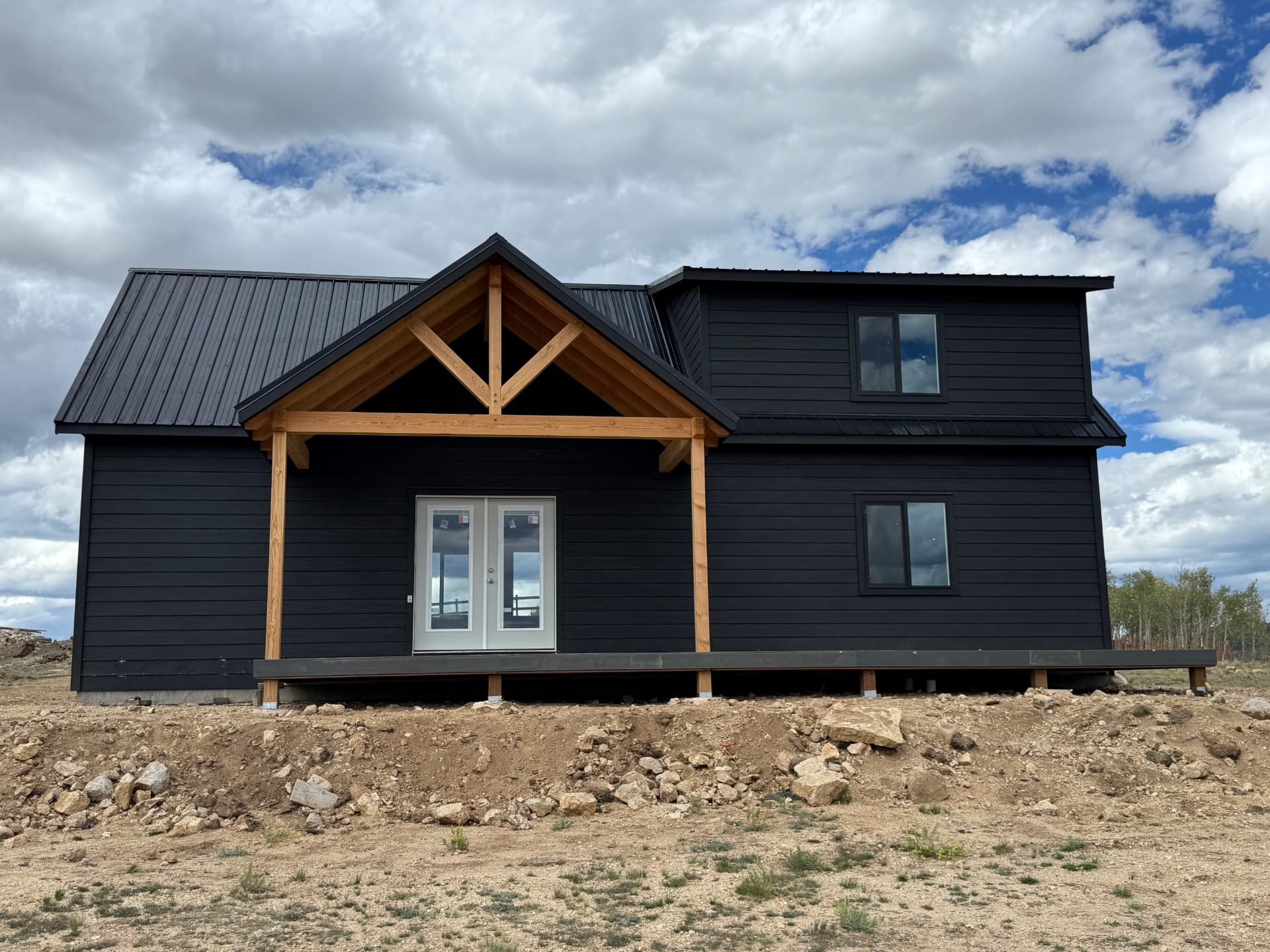 Finished black Sunny Side home shell with standing seam metal roof and timber frame porch in Jefferson, Colorado