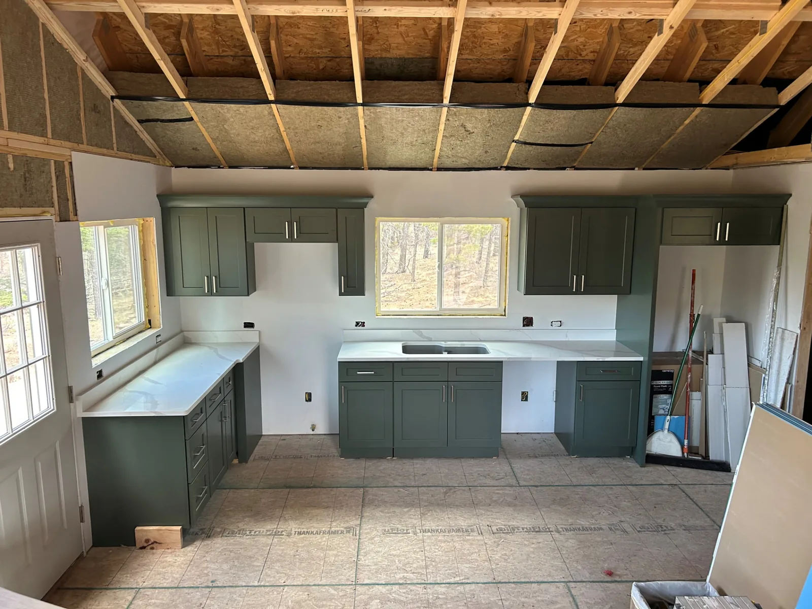 Green kitchen cabinetry and exposed ceiling insulation during Fort Garland homeshell finishing