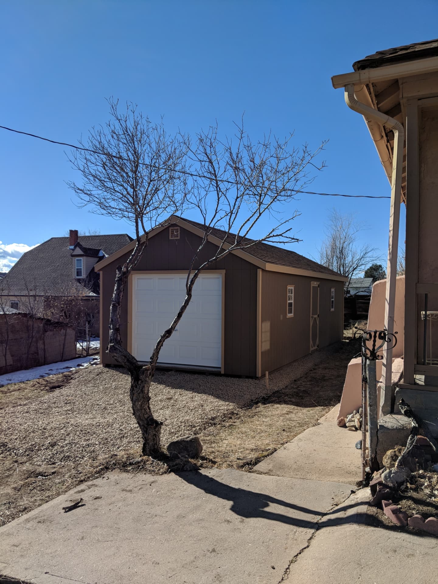 Brown one-car garage placed beside a Colorado home with a gravel approach