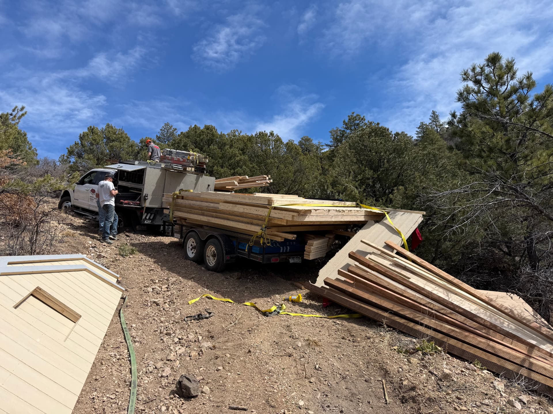 Shed Yard crew beside the truck and trailer on a steep dirt road after building materials slid off the trailer