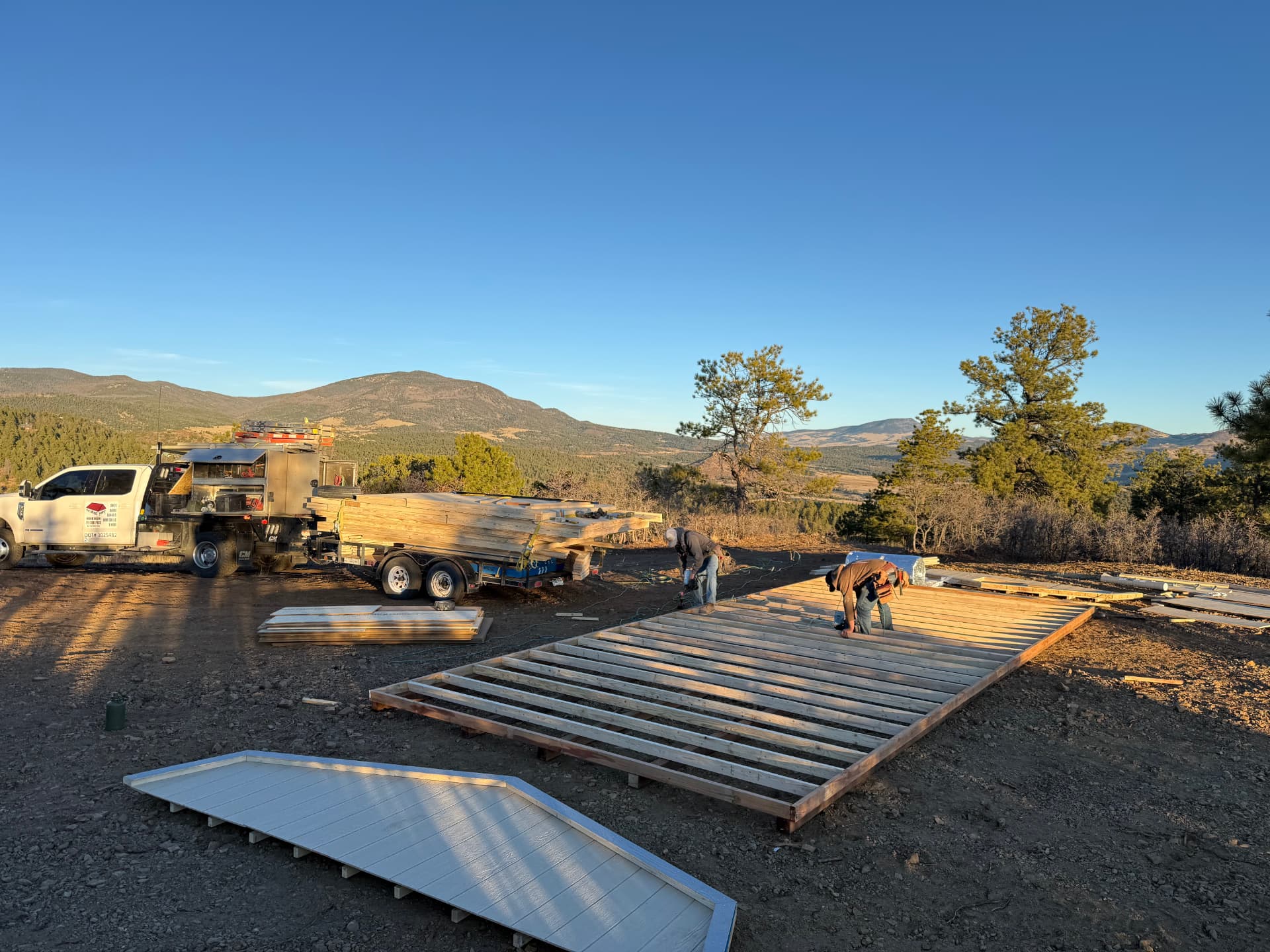 Two crew members framing the subfloor of a 14x32 Hi Wall Barn on site with mountains behind, near Canon City, Colorado