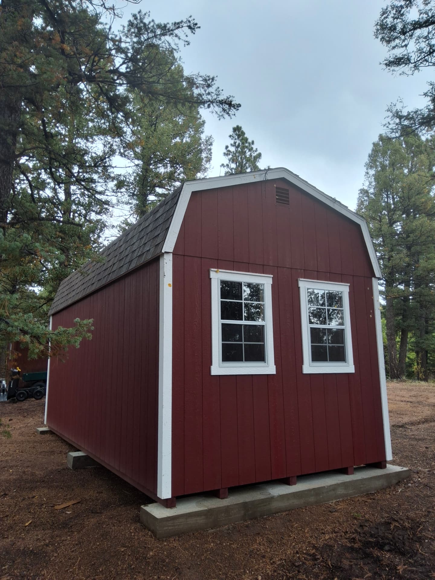 Back of a 10x20 barn with two 24x36 windows, raised on concrete piers over sloped ground in Woodland Park