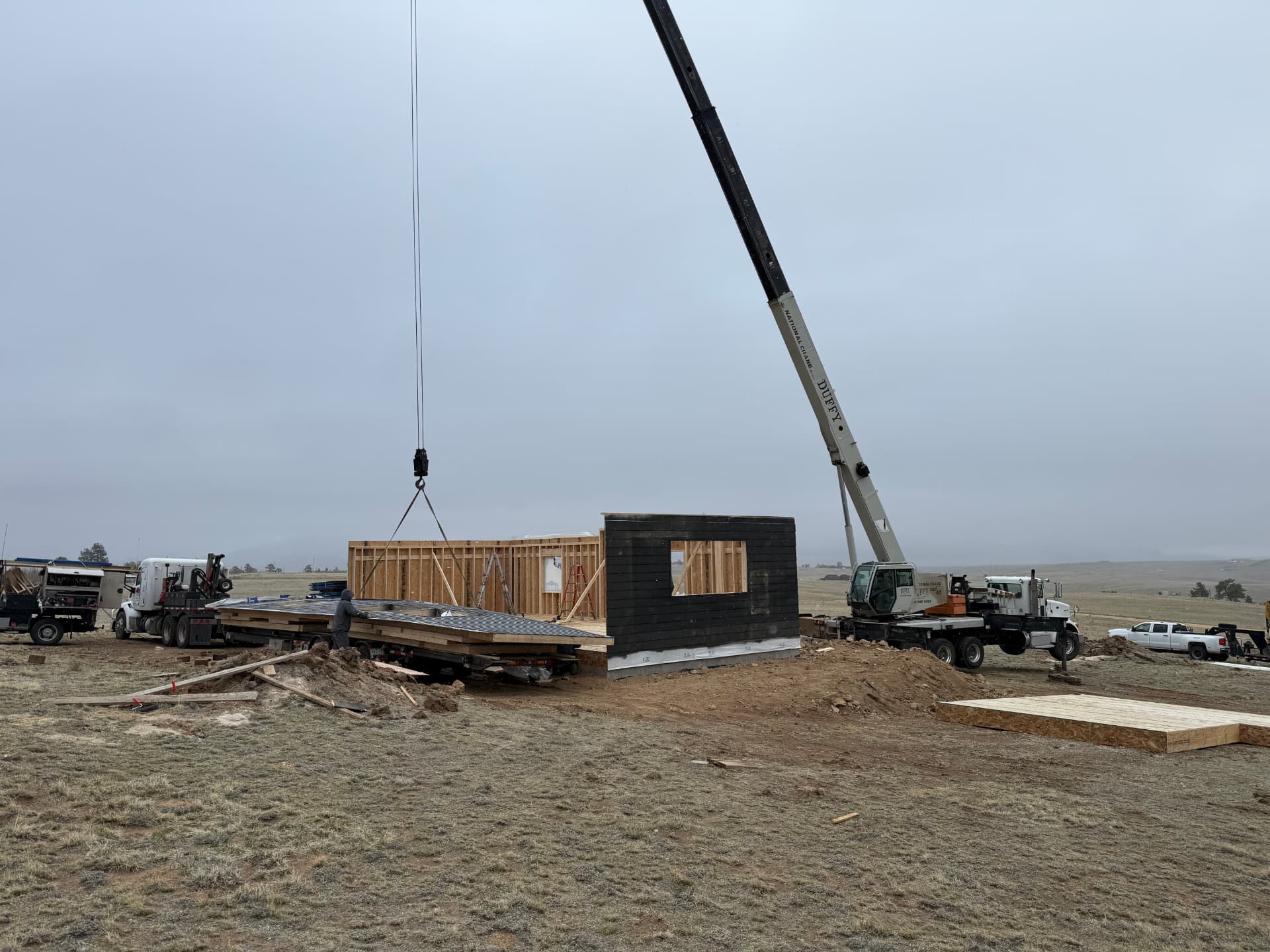 Crane setting a framed and sided wall panel on a Sunny Side home shell foundation near Jefferson, Colorado