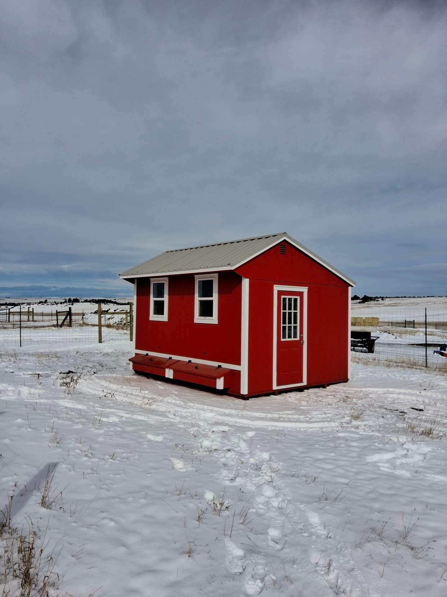 Red gable shed with white trim and a metal roof built to shed snow, sitting in a snow-covered Colorado field