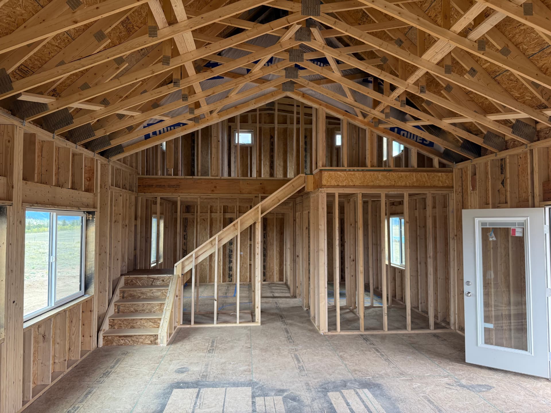 Interior of a Sunny Side home shell in Jefferson Colorado showing open framing, vaulted trusses, stairs to the 20x10 bonus loft and French doors