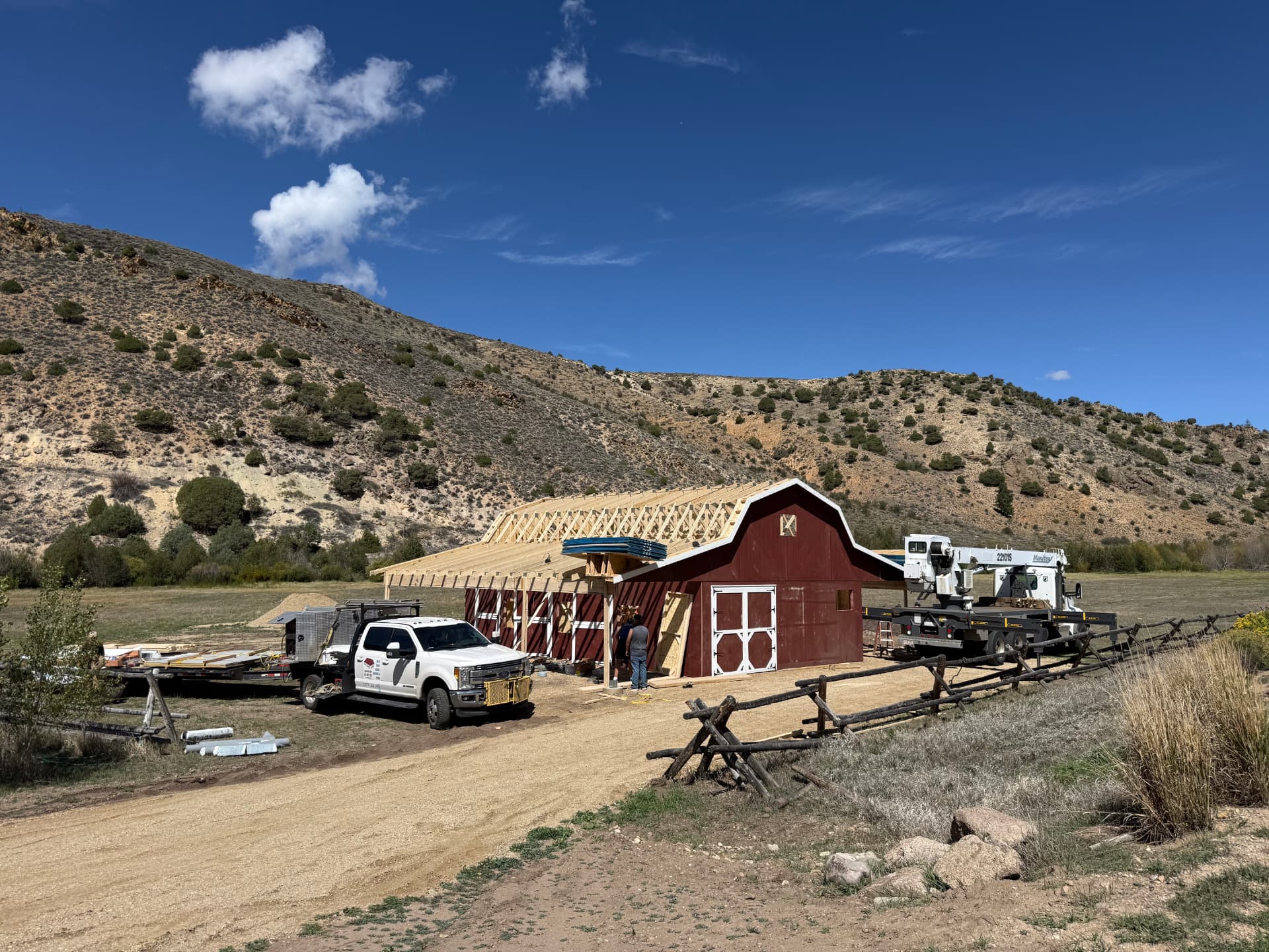 Custom red Hi Wall Barn under construction in Parshall, Colorado with roof framing and equipment on site