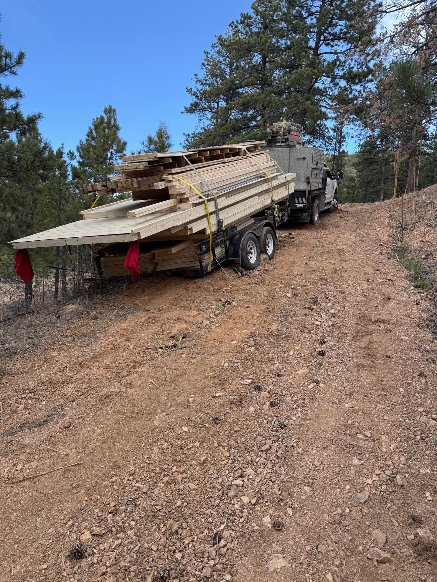 Truck pulling a re-secured trailer of building materials up a rocky dirt road toward a hilltop job site in Colorado