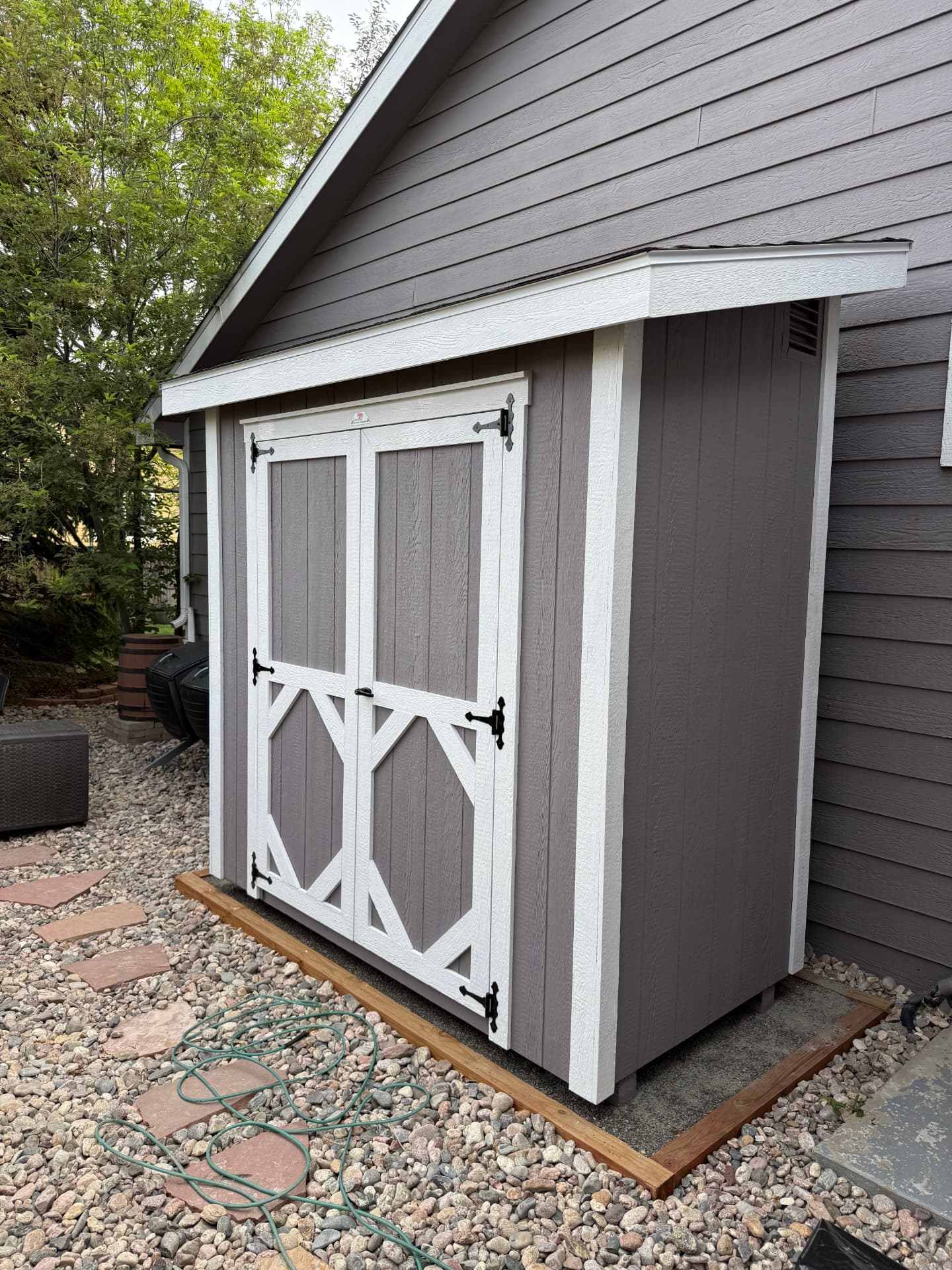 Gray storage shed with white trim set on a level base beside a house in a Colorado backyard