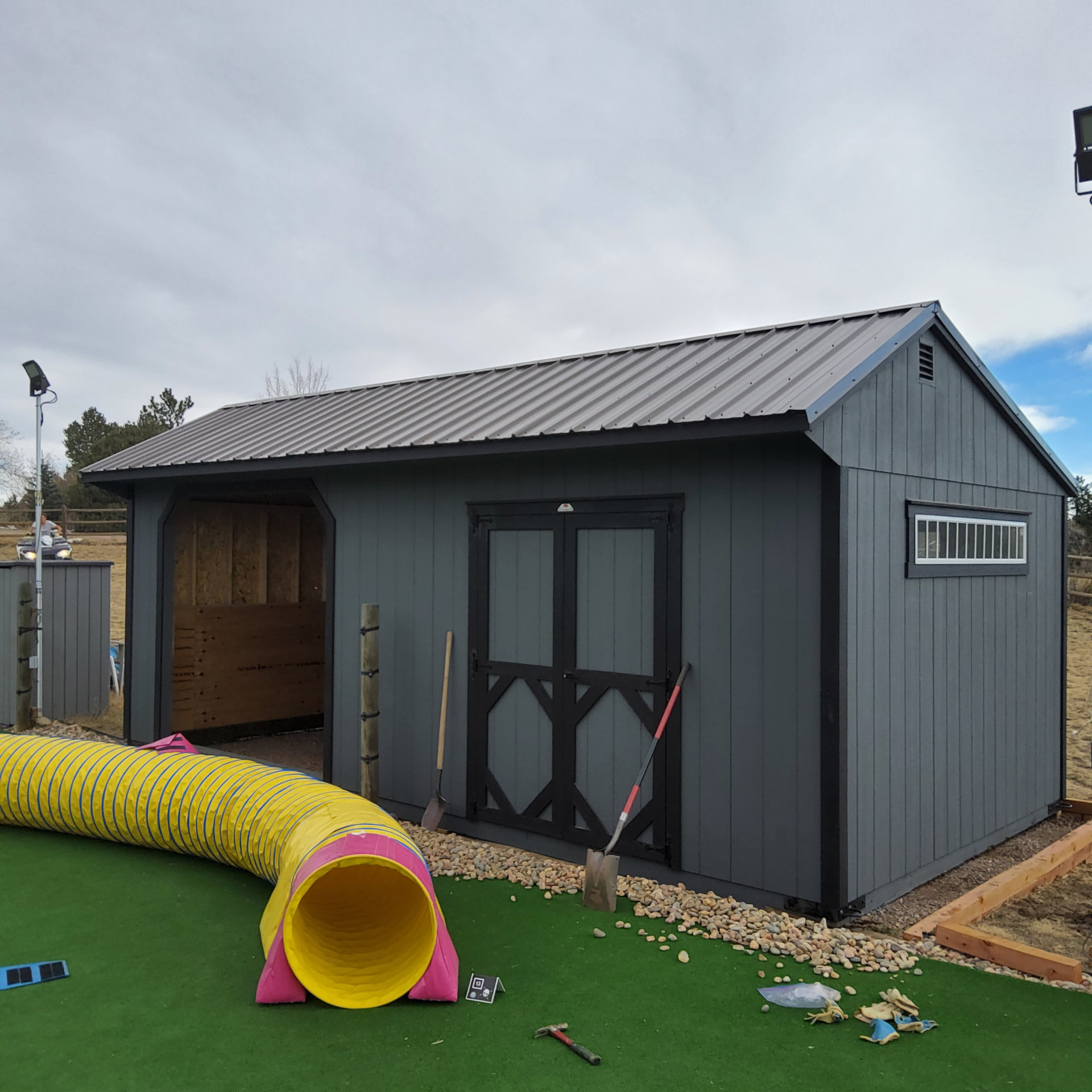 Gray loafing shed with dark metal roof, open front, and side door installed on a prepared site in Colorado