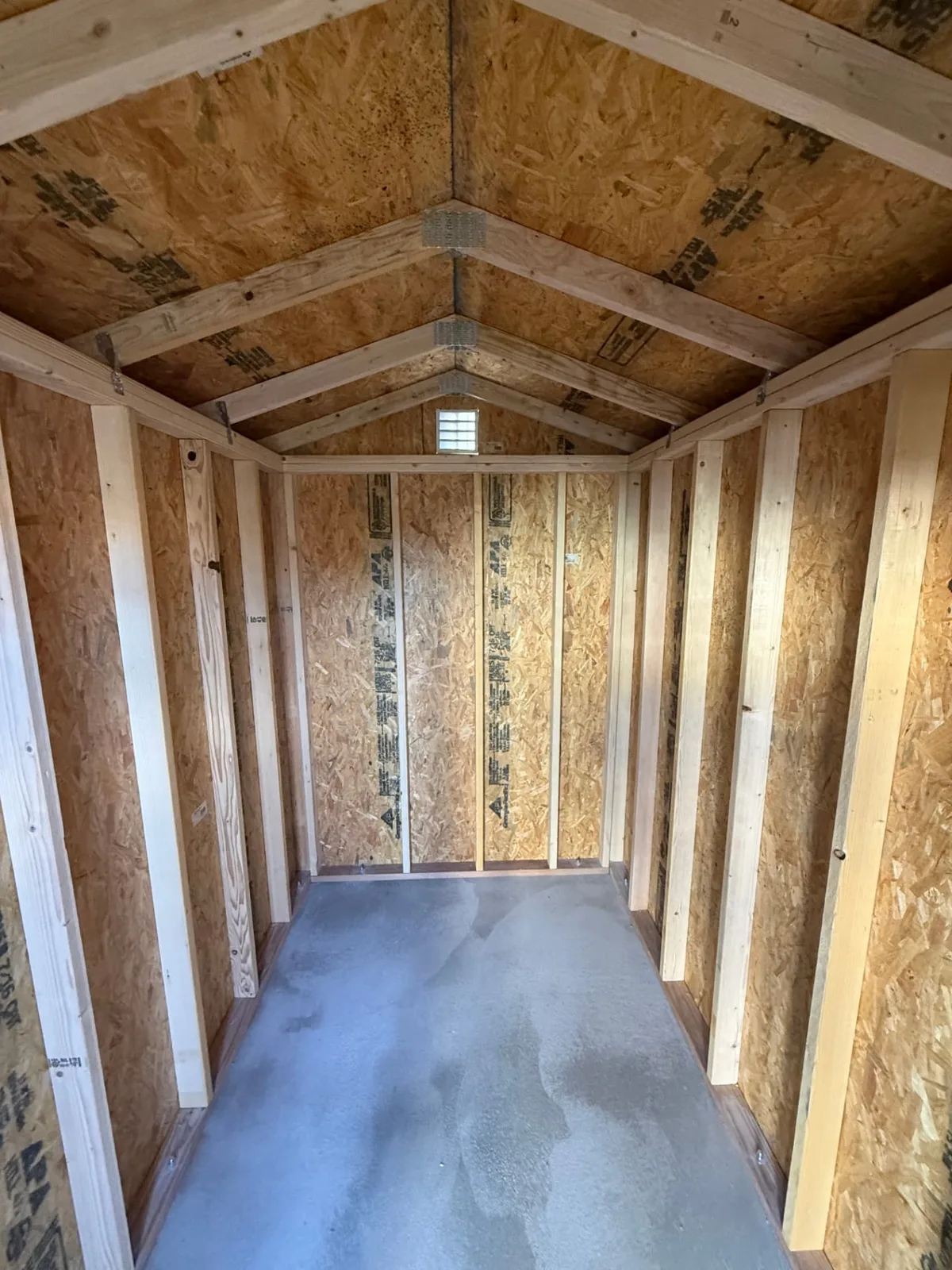 Unfinished shed interior with exposed wood framing, pitched roof and concrete floor