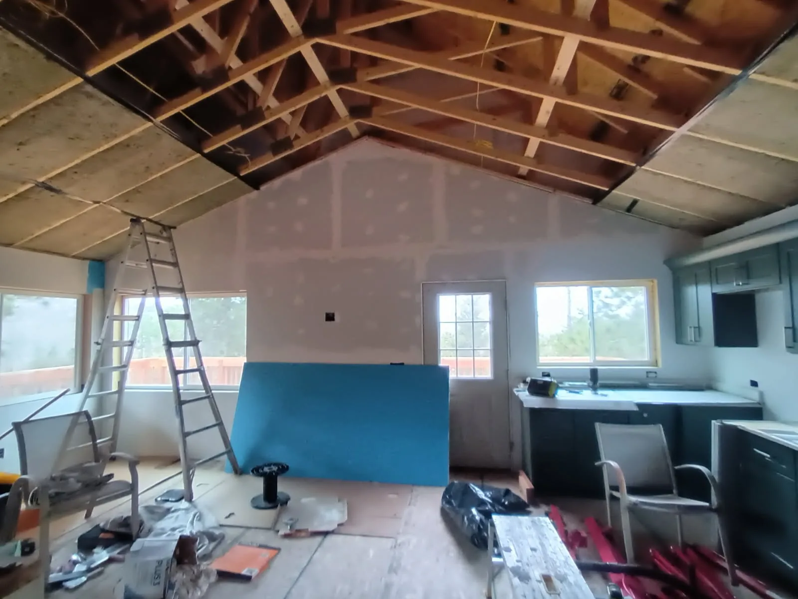 Drywall, ladders and exposed roof trusses during Fort Garland homeshell interior finishing